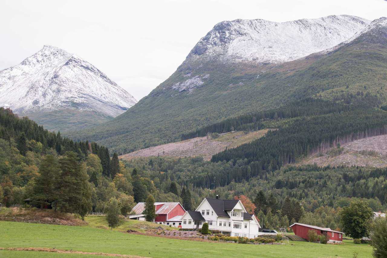 Gård med snødekte fjell og skog i bakgrunn